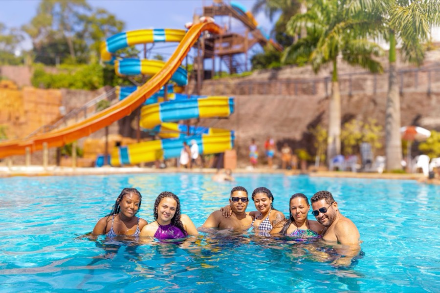 Família sorrindo na piscina do Blue Beach, com os toboáguas ao fundo